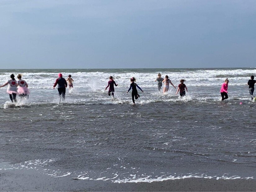 une photo d'un groupe de personness qui cours vers la mer en journée d'hiver